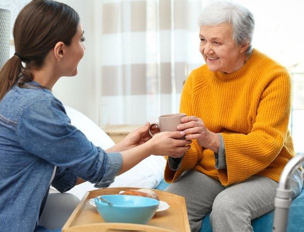 Young Woman Handing Cup to Smiling Elderly Woman in Bright Room