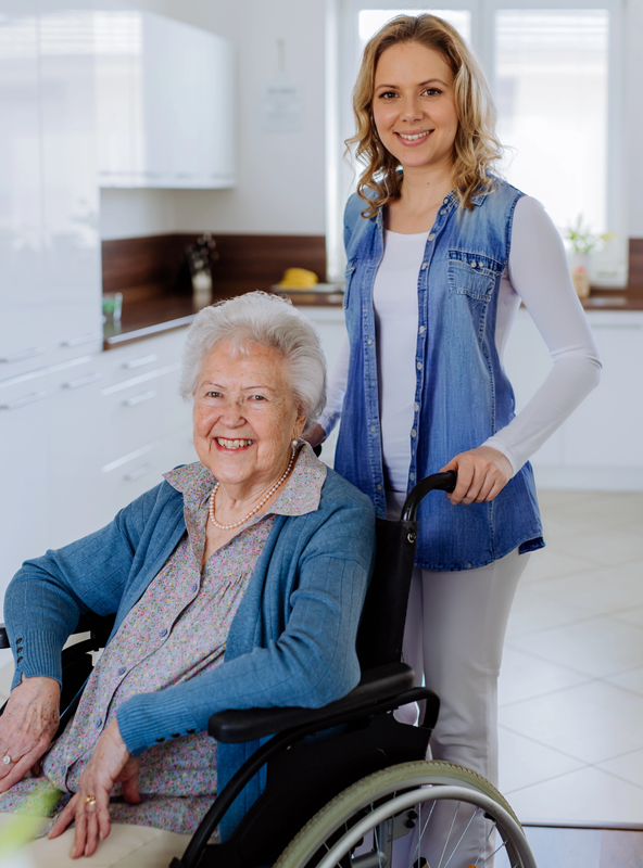 Smiling Elderly Woman in Wheelchair with Caregiver in a Bright Kitchen