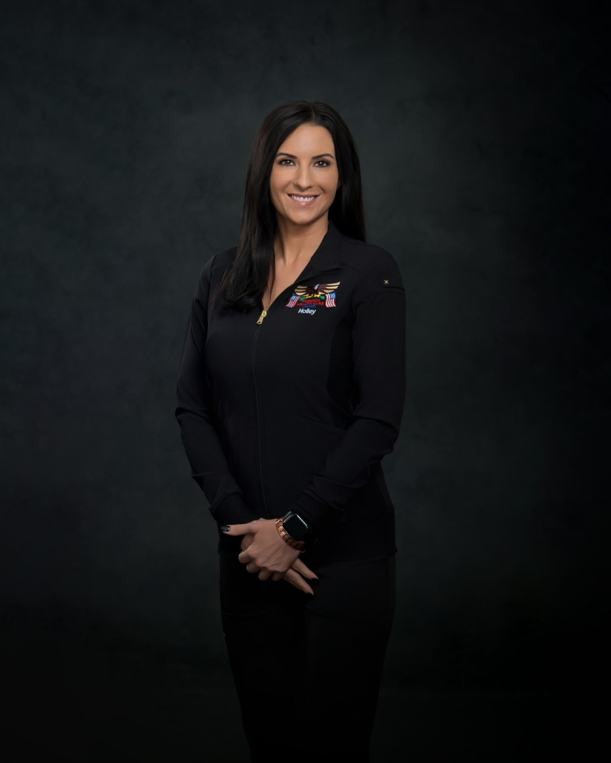 Smiling Woman in Black Zip-Up Jacket Standing Against Dark Background